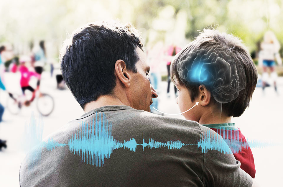A father talking to his young son, who wears a hearing aid