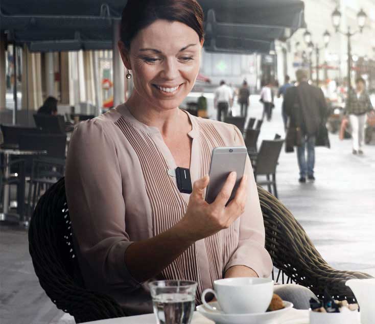 A woman wearing hearing aids smiles while using her phone